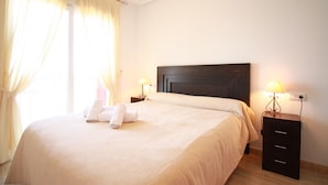 Uma cama bem arrumada com toalhas, uma cabeceira escura e abajures laterais.