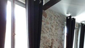 A room with a rustic stone wall, a wooden planter with branches, and black curtains tied with gold chains.