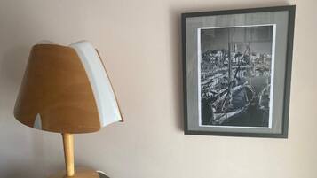 A lamp with a wooden shade and a framed black and white photograph of a harbor scene on the wall.