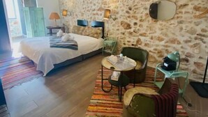 A bedroom with a bed, a small table, a chair, and a stone wall.