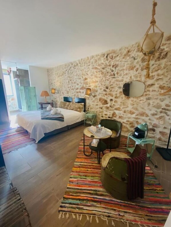 Quarto com cama, uma mesinha, uma cadeira e parede de pedra.