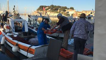 Una marina con barche ormeggiate, persone al lavoro e edifici sullo sfondo.