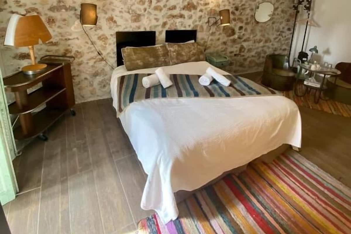 Ein Schlafzimmer mit Stehwand, einem Bett mit gestreifter Bettdecke, zwei Nachttischlampen, einem kleinen Tisch mit Lampe und einem farbenfrohen Streifen Teppich.