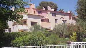Un immeuble à plusieurs étages, doté d’une façade rose, entouré de verdure et d’une clôture blanche.