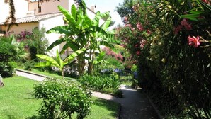 Un jardin avec un sentier, différentes plantes et un bâtiment en arrière-plan.