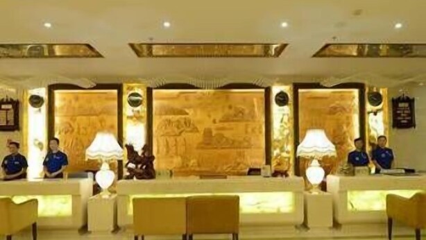 A reception area with a reception desk, two receptionists, and a seating area with chairs. - West Tour Hotel (Shanshan)