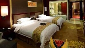 A hotel room with two beds, a desk, a chair, a fruit bowl, and a mirror. - West Tour Hotel (Shanshan)