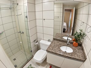 Een badkamer met een douchecabine van glas, een toilet en een wastafel met een granieten aanrechtblad.