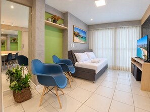 Uma sala de estar moderna com um sofá, duas poltronas azuis, uma televisão e um quadro de uma cena de praia.