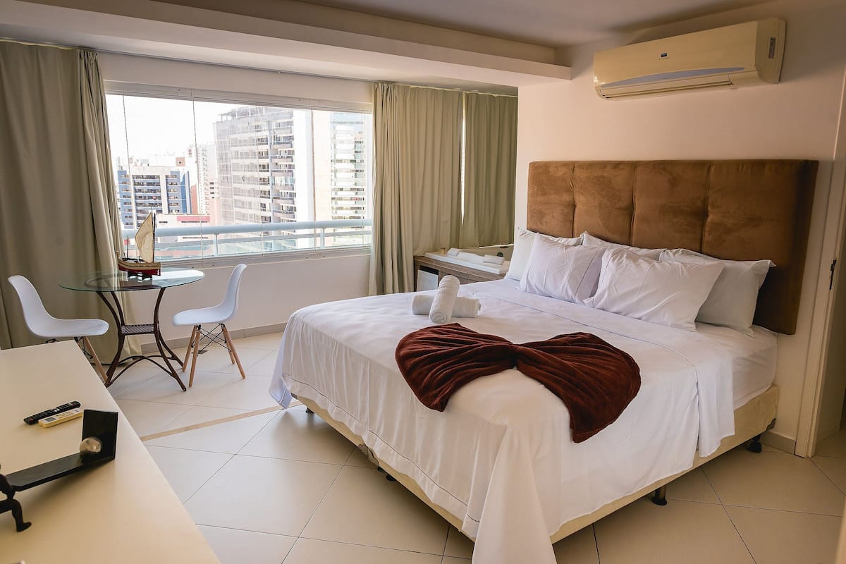 Une chambre d’hôtel avec un lit, un bureau, une chaise, une petite table et une fenêtre avec des rideaux.