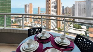 Ein Balkon mit Tisch für vier Personen, Blick auf eine Skyline mit Wolkenkratzern und den Ozean.