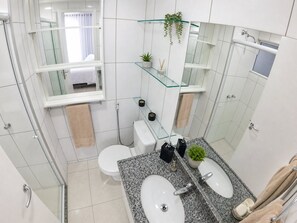 A modern bathroom with a glass shower enclosure, a white toilet, a granite countertop with a sink and mirror, and a small potted plant. - Apartamento Vista mar Praia de Iracema (Fortaleza)