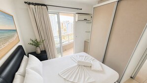 Ein Hotelzimmer mit einem Bett, einem Nachttisch, einer Topfpflanze und Blick auf die Stadt durch das Fenster.