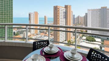 Varanda com mesa posta para quatro pessoas, vista para um horizonte urbano com arranha-céus e mar.
