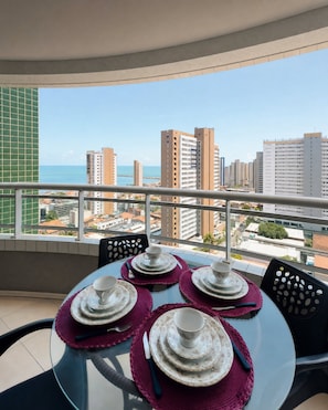 A balcony with a table set for four, overlooking a cityscape with high-rise buildings and a view of the sea. - Apartamento Vista mar Praia de Iracema (Fortaleza)
