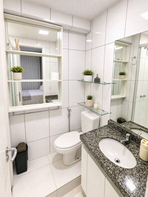 A modern bathroom with a toilet, sink, and glass shelves with plants. - Apartamento Vista mar Praia de Iracema (Fortaleza)