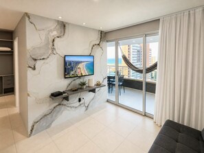A modern living room with a marble wall, a flat-screen TV, a sofa, and a balcony with a hammock. - Apartamento Vista mar Praia de Iracema (Fortaleza)