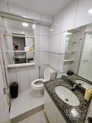 A modern bathroom with a toilet, sink, and glass shelves. - Apartamento Vista mar Praia de Iracema (Fortaleza)