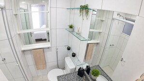 Ein modernes Badezimmer mit Duschkabine aus Glas, einer weißen Toilette, einer Arbeitsplatte aus Granit mit Waschbecken und Spiegel sowie einer kleinen Topfpflanze.