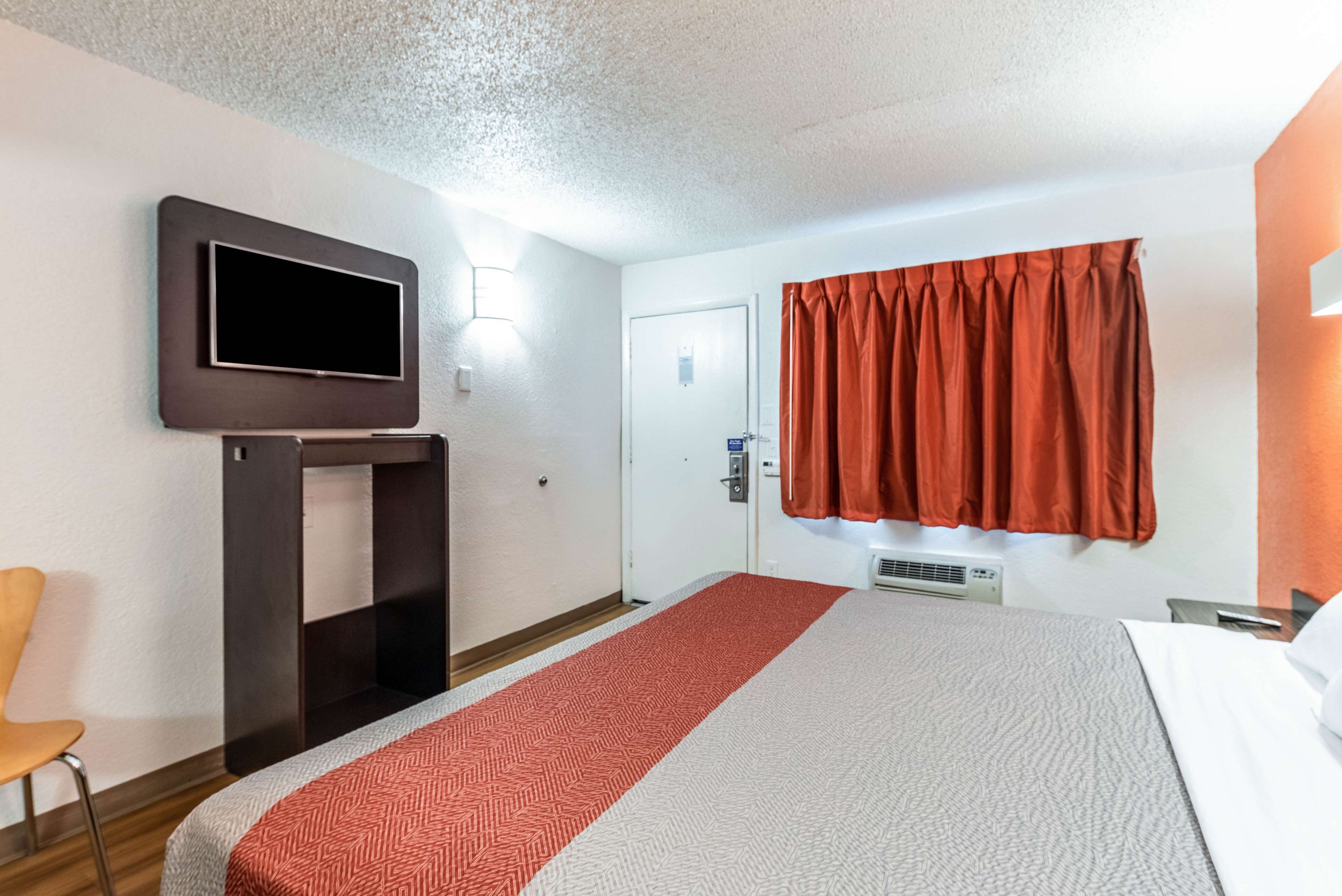 Ein Hotelzimmer mit Bett, Wandfernseher, Schreibtisch mit Stuhl und einem Vorhangfenster.