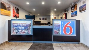 Ein Empfangsbereich mit einem Tresen, einem Computer und verschiedenen Schildern, darunter ein 'Motel 6'-Schild.