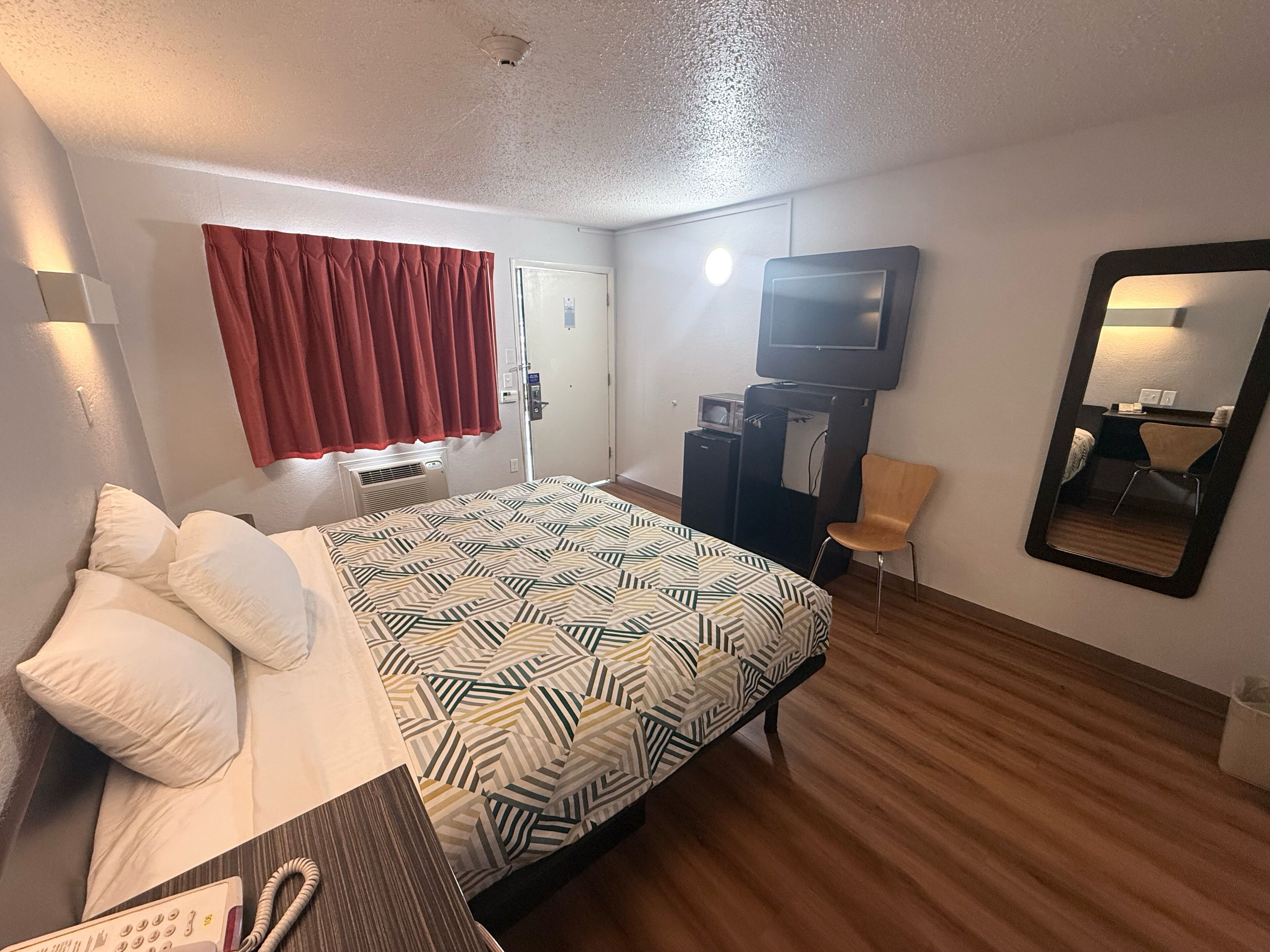 Una habitación de hotel con cama, escritorio, silla, televisor, espejo y puerta.