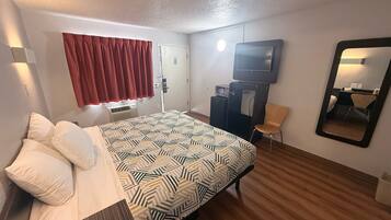 Una habitación de hotel con cama, escritorio, silla, televisor, espejo y puerta.