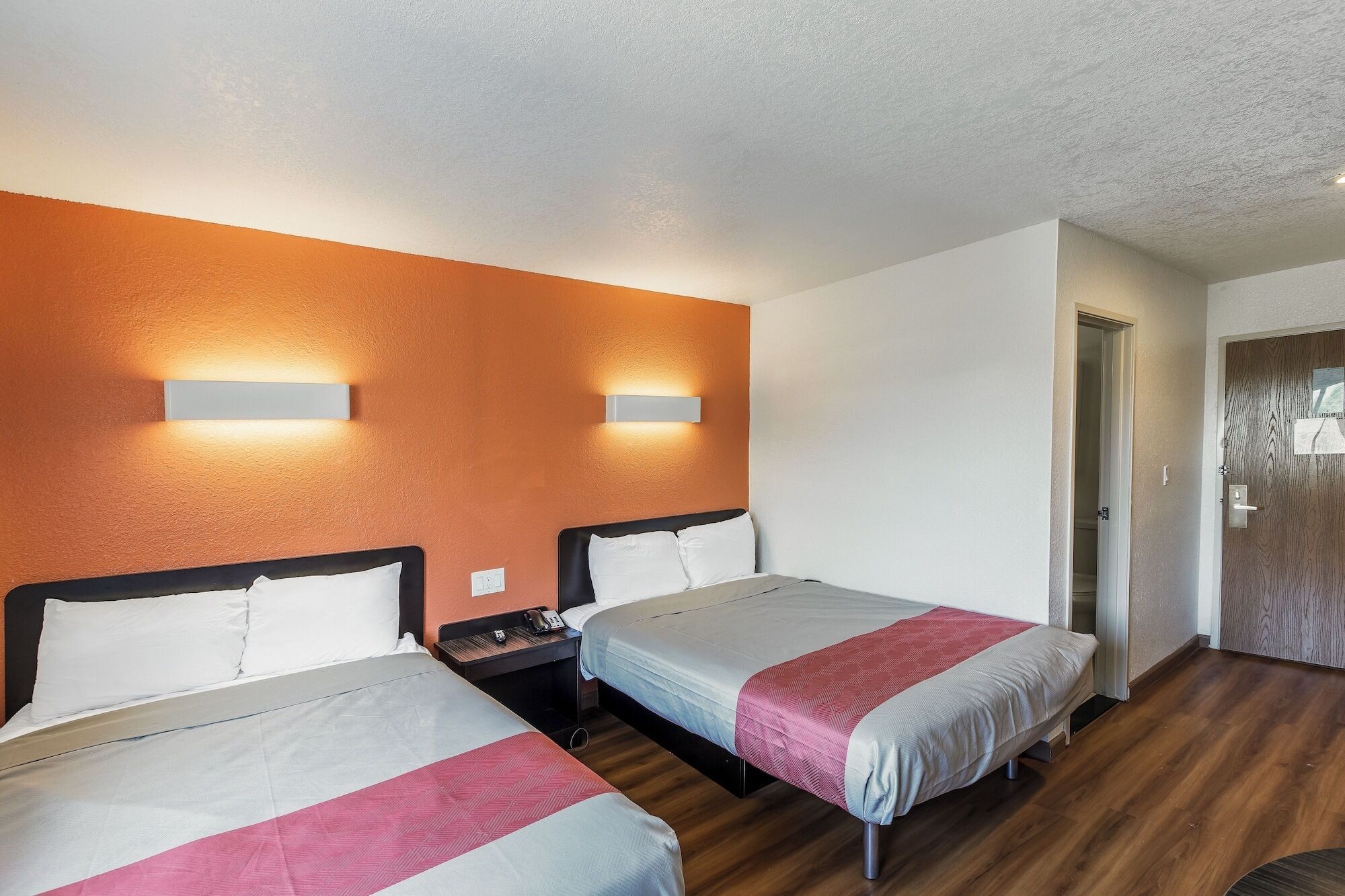 A hotel room with two beds, a wooden floor, and a door leading to a bathroom.