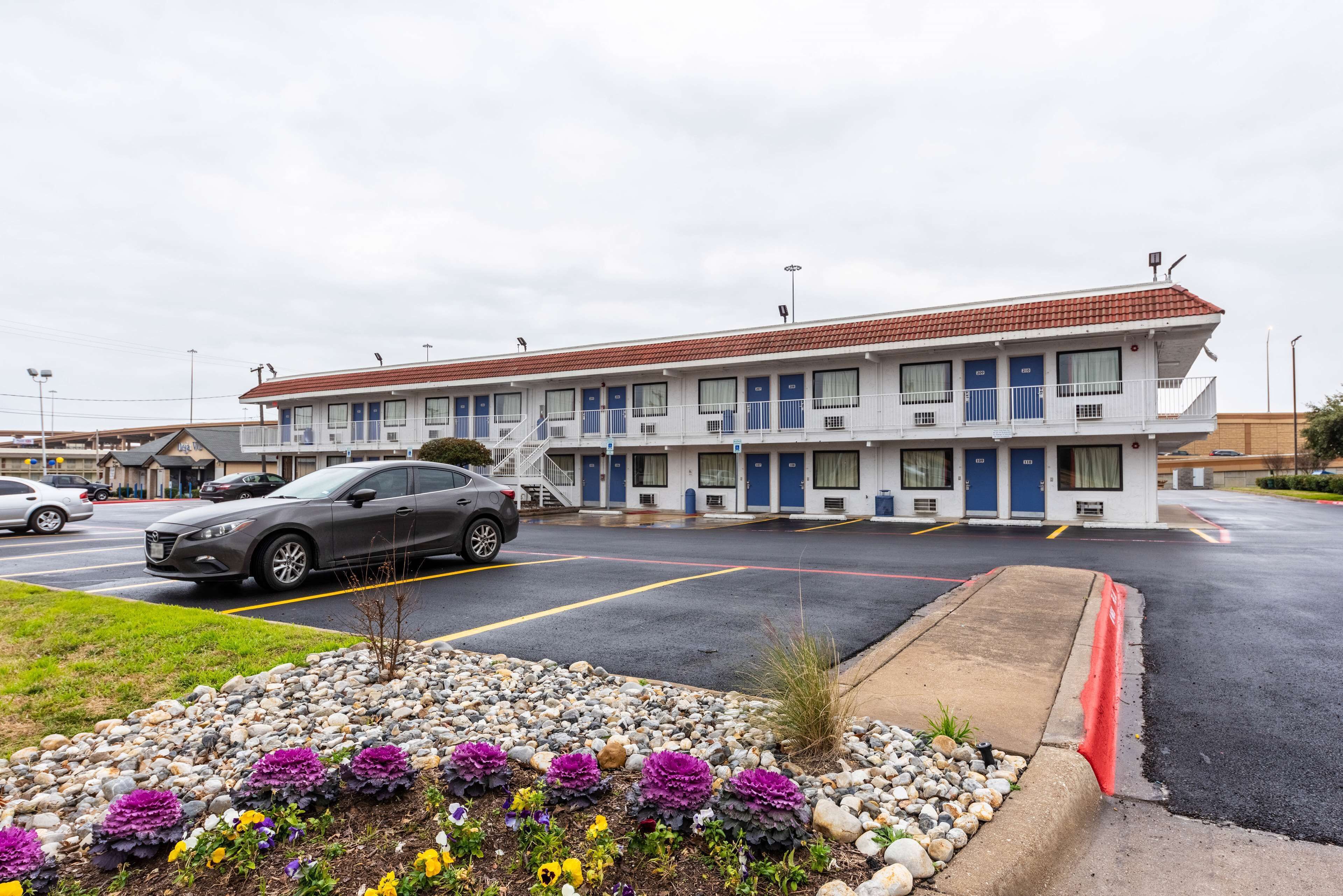 A motel with multiple rooms, a parking lot, and a landscaped area with flowers.