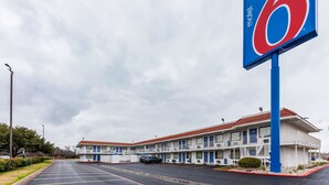 Ein Motel mit großer blauer Schrifttafel, mehreren Zimmern und einem Parkplatz.