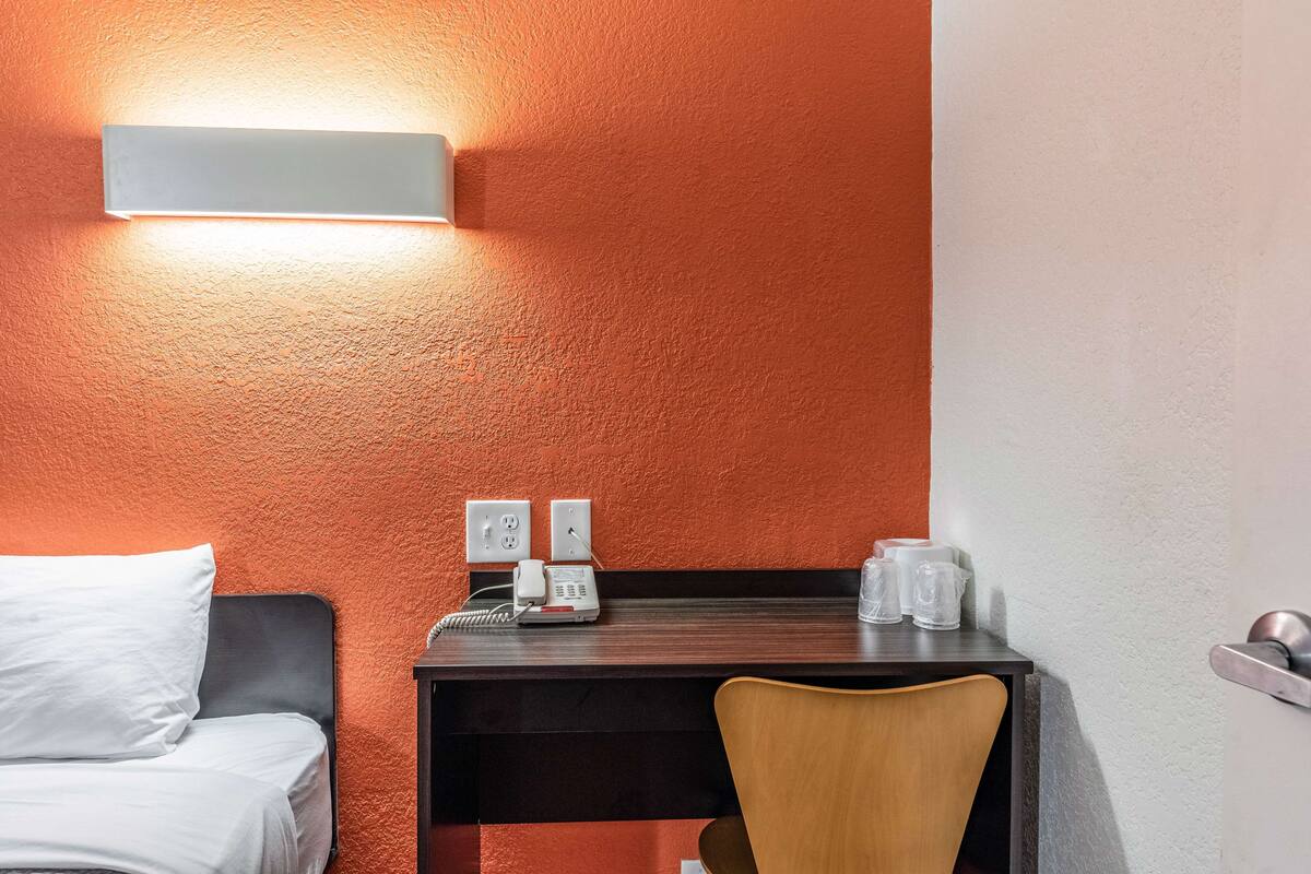 Ein Hotelzimmer mit einem Bett, einem Schreibtisch mit Telefon und Brille sowie einem Stuhl.