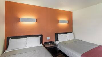 A hotel room with two beds, a nightstand with a phone, and wall-mounted lighting.