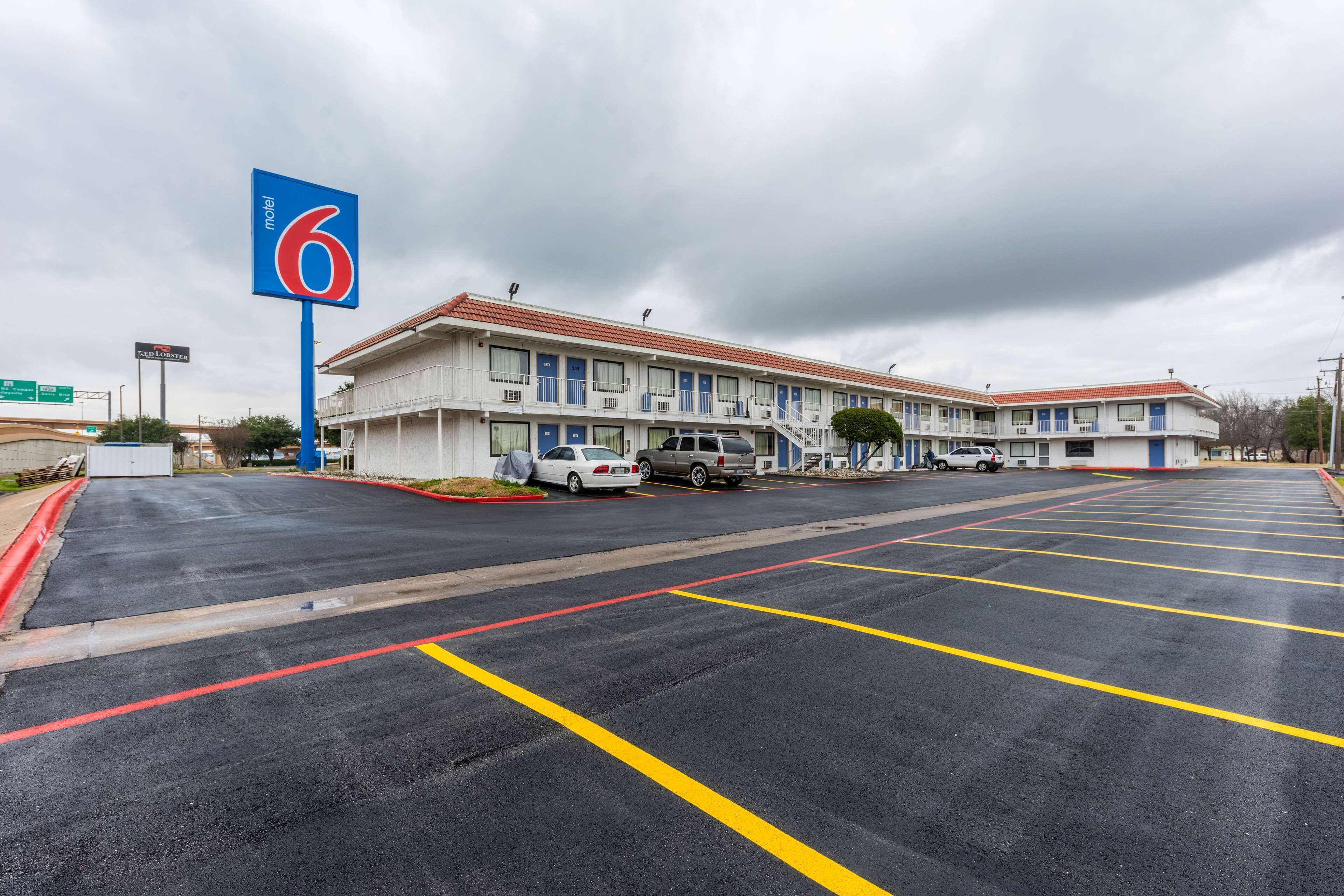 A motel with a large sign, multiple parking spaces, and a building with a red roof.