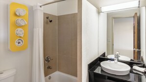 Ein Badezimmer mit einer Badewanne, einem Waschbecken mit Spiegel und einer Dusche mit Duschvorhang. Gelbe Handtücher hängen an einem Ablagegestell.