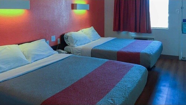 Two single beds with striped bedding in a room with a red wall and a window with red curtains.