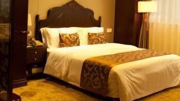 A hotel room with a large bed, a bedside table, a lamp, and a window with curtains. - Hailan Hotel (Wuxi)