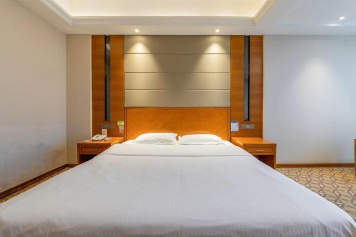 Quarto de hotel com uma cama grande, cabeceira de madeira, mesas de cabeceira e piso estampado.