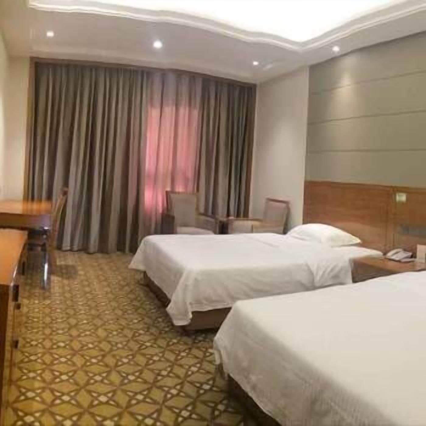 A hotel room with two beds, a desk, a chair, and a large window with curtains.