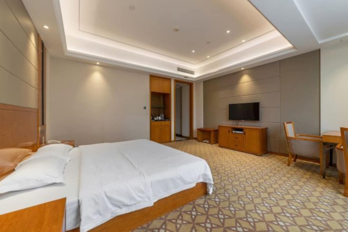 Quarto de hotel com cama, escrivaninha, televisão e guarda-roupa.