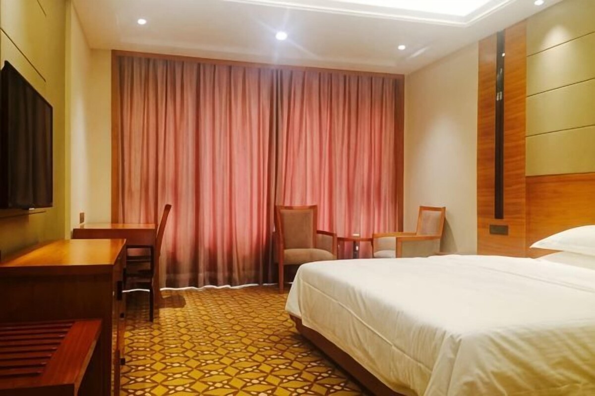 A hotel room with a bed, a desk, a chair, a television, and a large window with curtains.