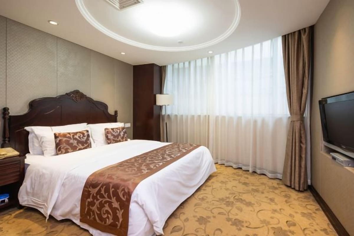 A hotel room with a large bed, a television, a nightstand, and a window with curtains.