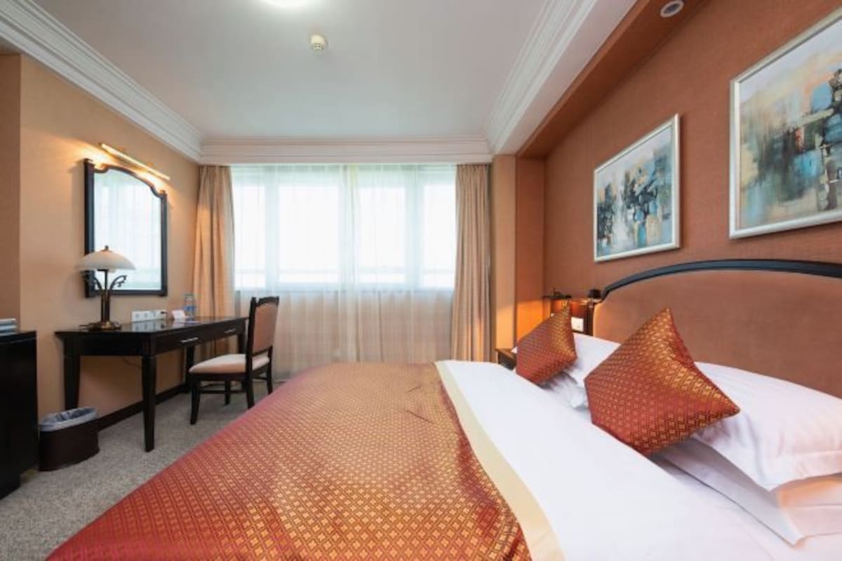 Quarto de hotel com cama, escrivaninha, cadeira, espelho e duas pinturas na parede.