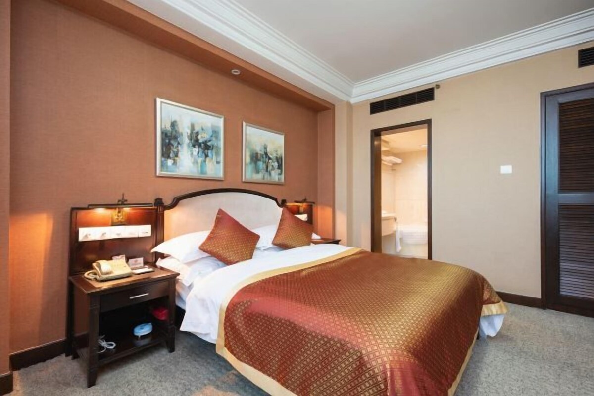 A hotel room with a large bed, a nightstand with a phone, and two framed pictures on the wall.