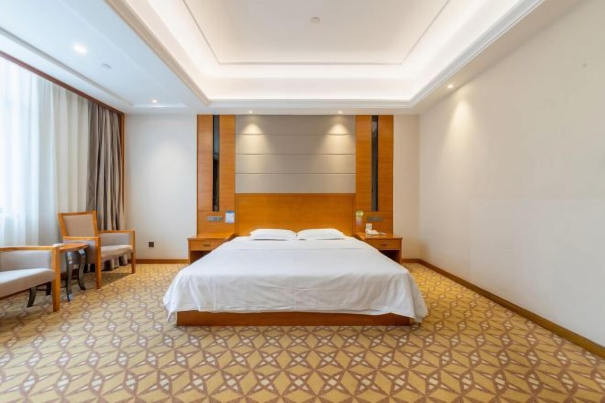 A hotel room with a large bed, a nightstand, a chair, and a desk.
