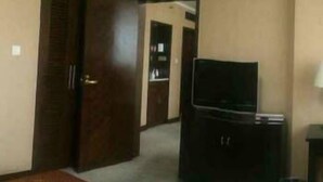 A hotel room with a single bed, a television on a stand, a wardrobe, and a small table with a lamp. - Hailan Hotel (Wuxi)