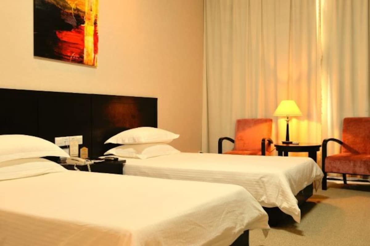 Quarto de hotel com duas camas de solteiro, uma mesa de cabeceira, um abajur, uma cadeira e um quadro na parede.