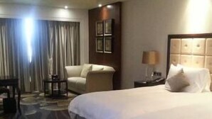 A hotel room with a large bed, a chair, a desk, and a lamp.