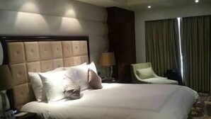 A hotel room with a large bed, a nightstand with a lamp, a chair, and a window with curtains.