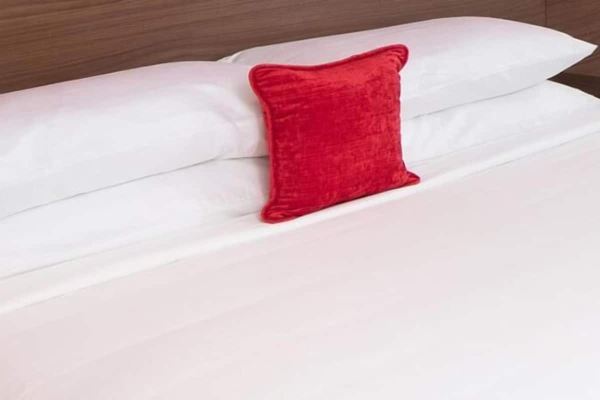 A bed with white bedding and a single red pillow.