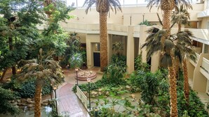 Un atrium interior amb una font central, envoltat de palmeres i diferents plantes.